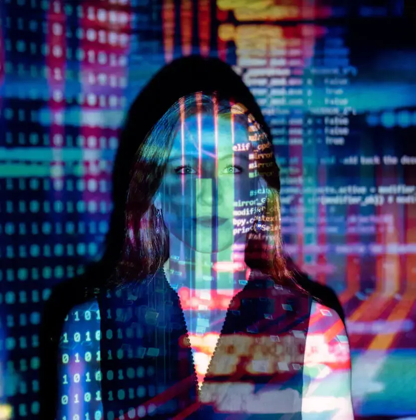 A woman standing with the reflection of many different screens displayed across her face that make her harder to see.